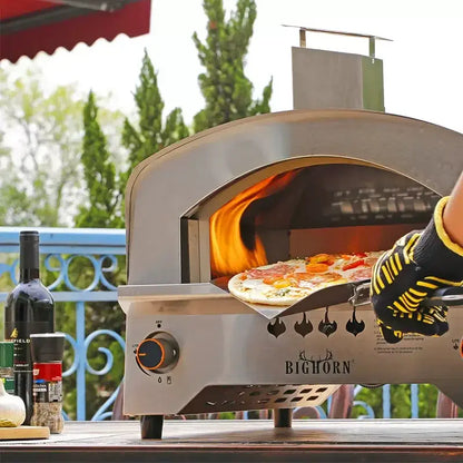 Large gas pizza oven in action outdoors, showcasing pizza being removed with a pizza paddle by a gloved hand.